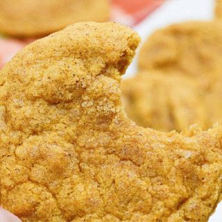 A person holding a pumpkin snickerdoodle with a bite taken out of it.