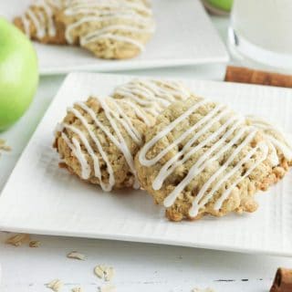 Oatmeal cookies with icing and apples on a white plate.