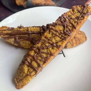 A plate with two chocolate dipped pumpkin biscotti on it.