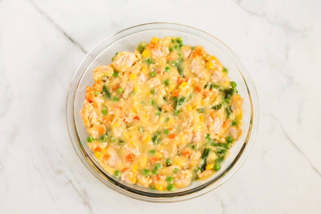 Glass bowl filled with a mixture of diced vegetables and chicken in a creamy sauce, placed on a marble surface.