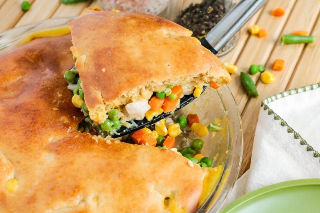 Turkey pot pie with cream of chicken soup recipe with a golden crust, filled with peas, carrots, corn, green beans, and chicken, in a glass dish with a slice being served on a spatula.