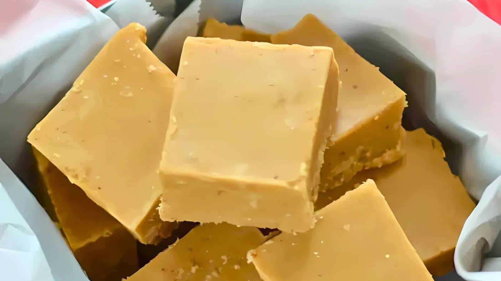 Close-up of several pieces of square-cut fudge stacked in a container lined with white paper.