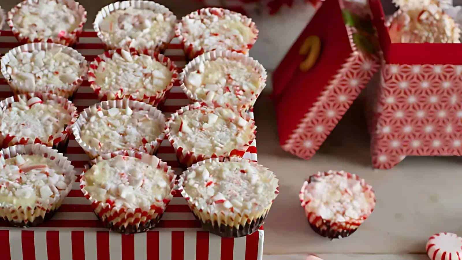 Festive red and white striped mini cupcake liners contain peppermint bark treats, arranged on a box with similar design. Some cupcakes are placed beside opened gift boxes with a pink pattern.