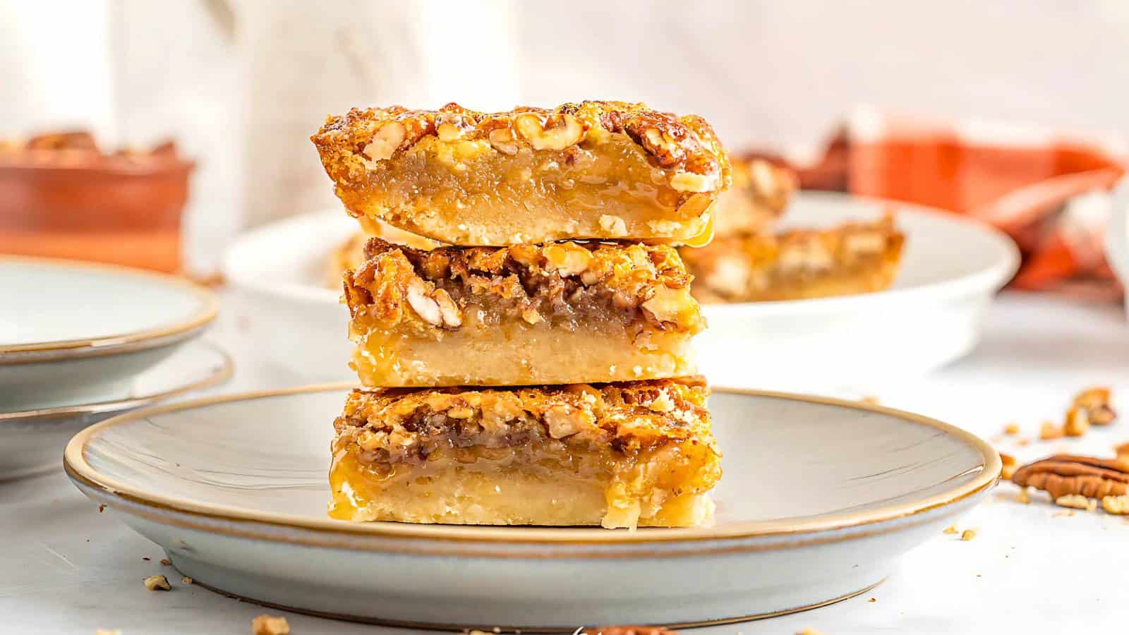 A stack of three pecan pie bars on a gray plate, with visible layers of crust, filling, and chopped pecans.