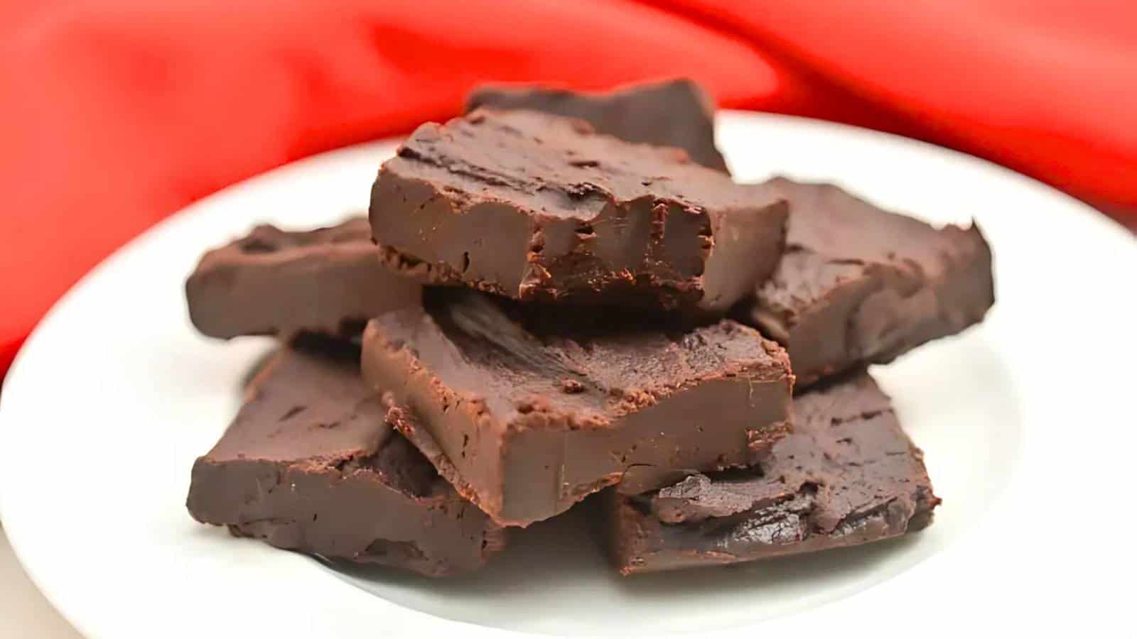 A white plate with a stack of thick, square chocolate fudge pieces against a red background.