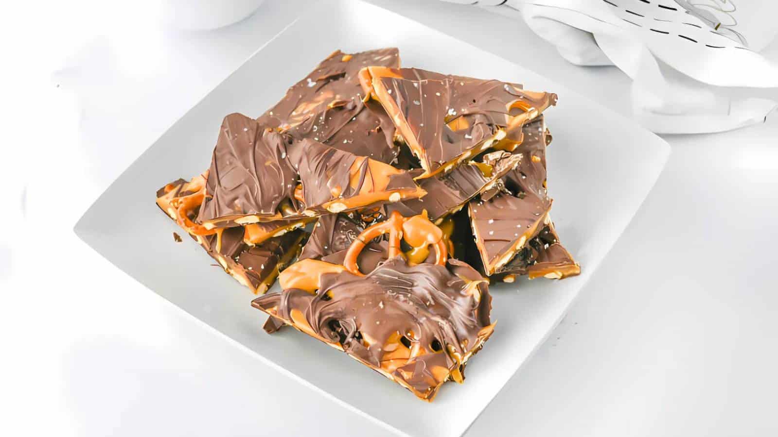 A plate of chocolate bark with caramel drizzles on a white background.