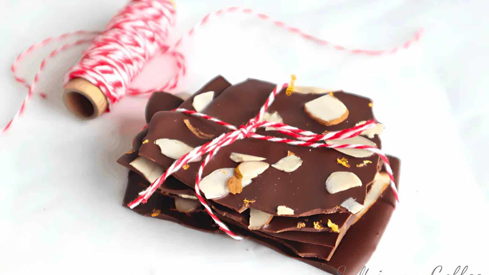 Pieces of chocolate bark with nuts wrapped in red and white twine, next to a spool of similar twine on a white surface.
