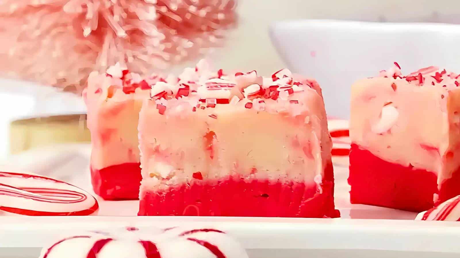 Close-up of red and white peppermint fudge squares on a plate, surrounded by peppermint candies.