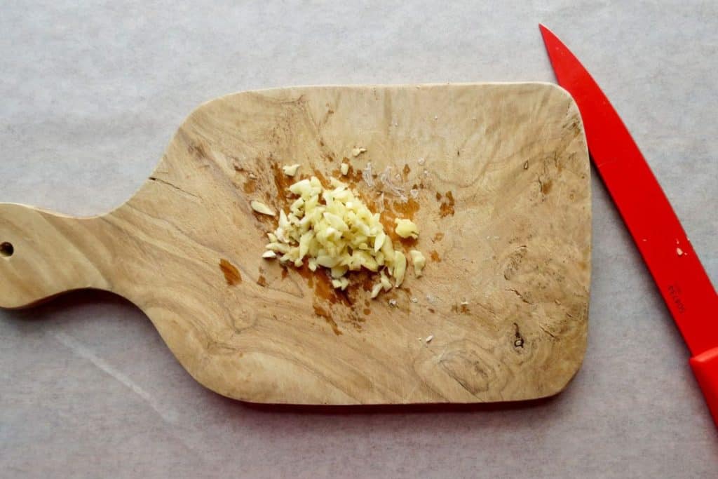 Chopped garlic on a wooden cutting board next to a red knife.