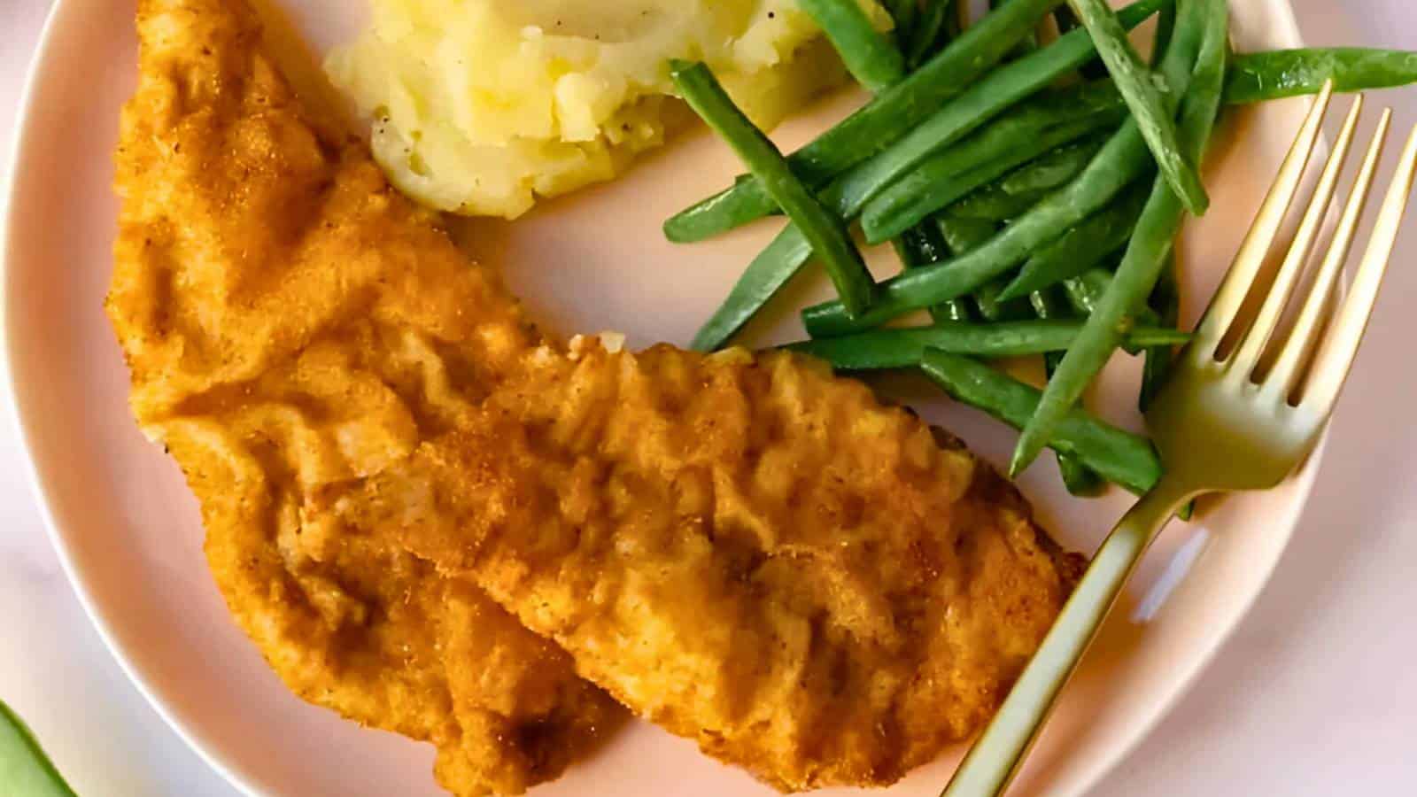 A plate with breaded chicken fillets, mashed potatoes, green beans, and a gold fork.