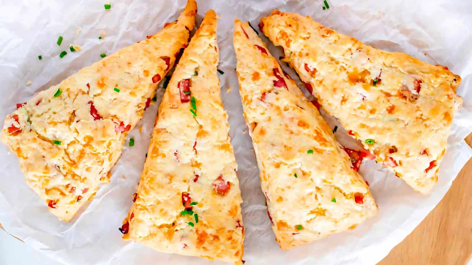 Four triangular bacon cheddar scones on parchment paper, garnished with chopped chives.
