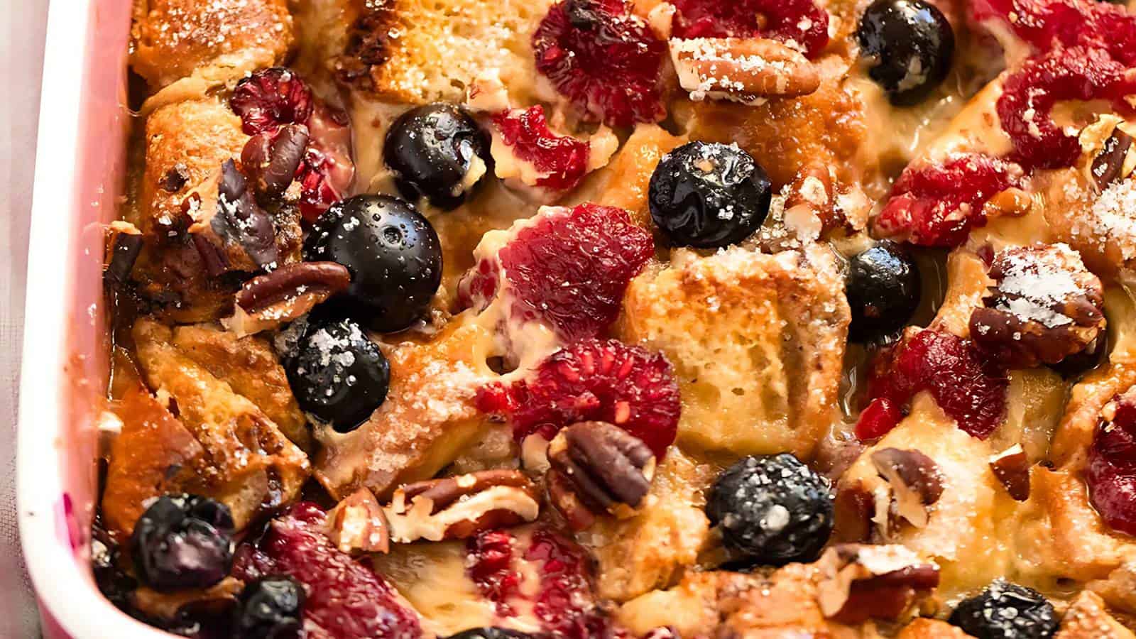 Baked French toast casserole with raspberries, blueberries, pecans, and a dusting of powdered sugar.