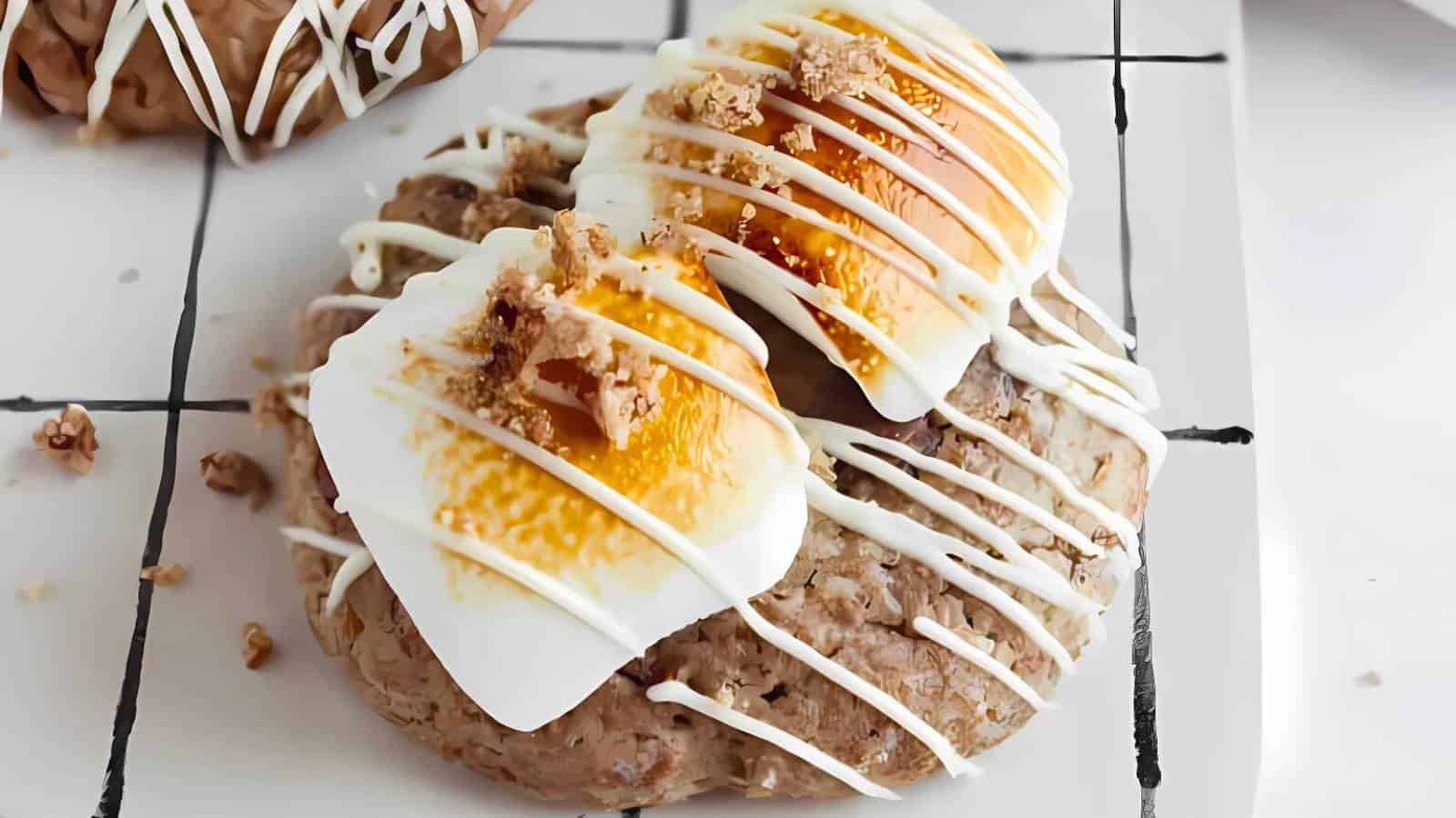 A pastry topped with two poached eggs, drizzled with white sauce, served on a white grid-patterned plate.