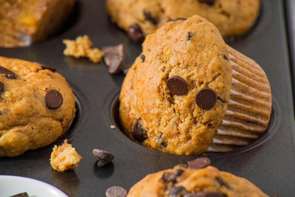 Peanut butter banana muffins in a baking tray, with some chocolate chips scattered around.