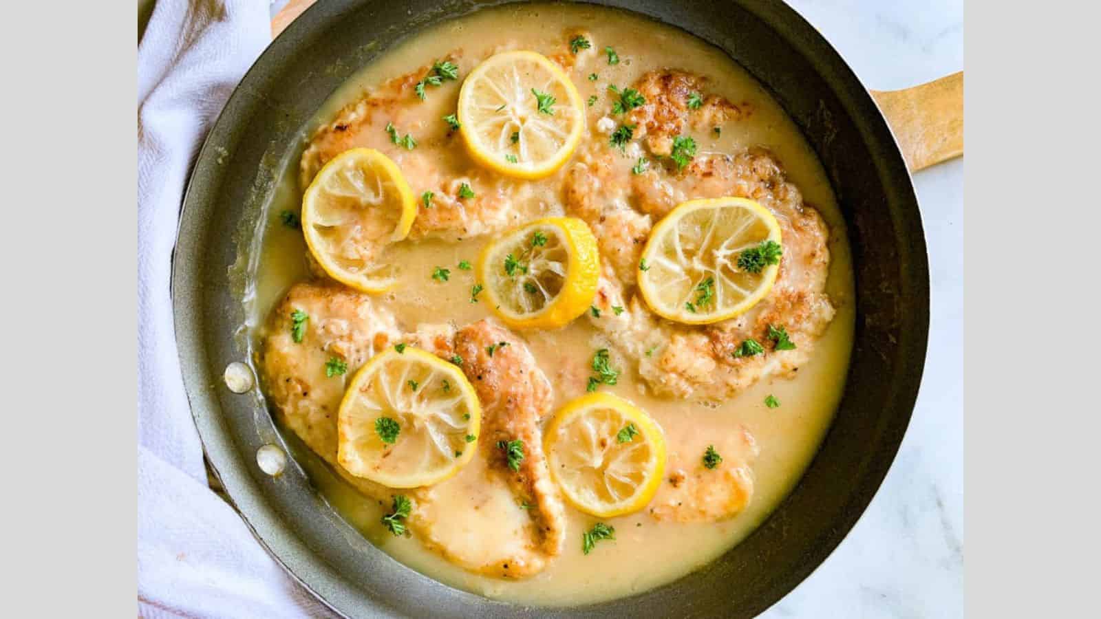 Pan of lemon chicken with sauce, topped with fresh lemon slices and parsley.