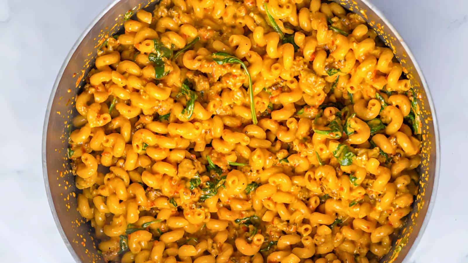 A skillet of cooked cavatappi pasta coated in a creamy orange sauce, garnished with fresh spinach leaves.