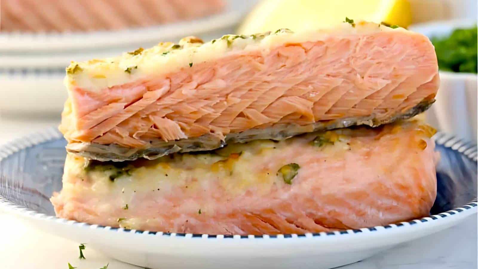 Two slices of cooked salmon, seasoned with herbs, are stacked on a blue-rimmed plate.