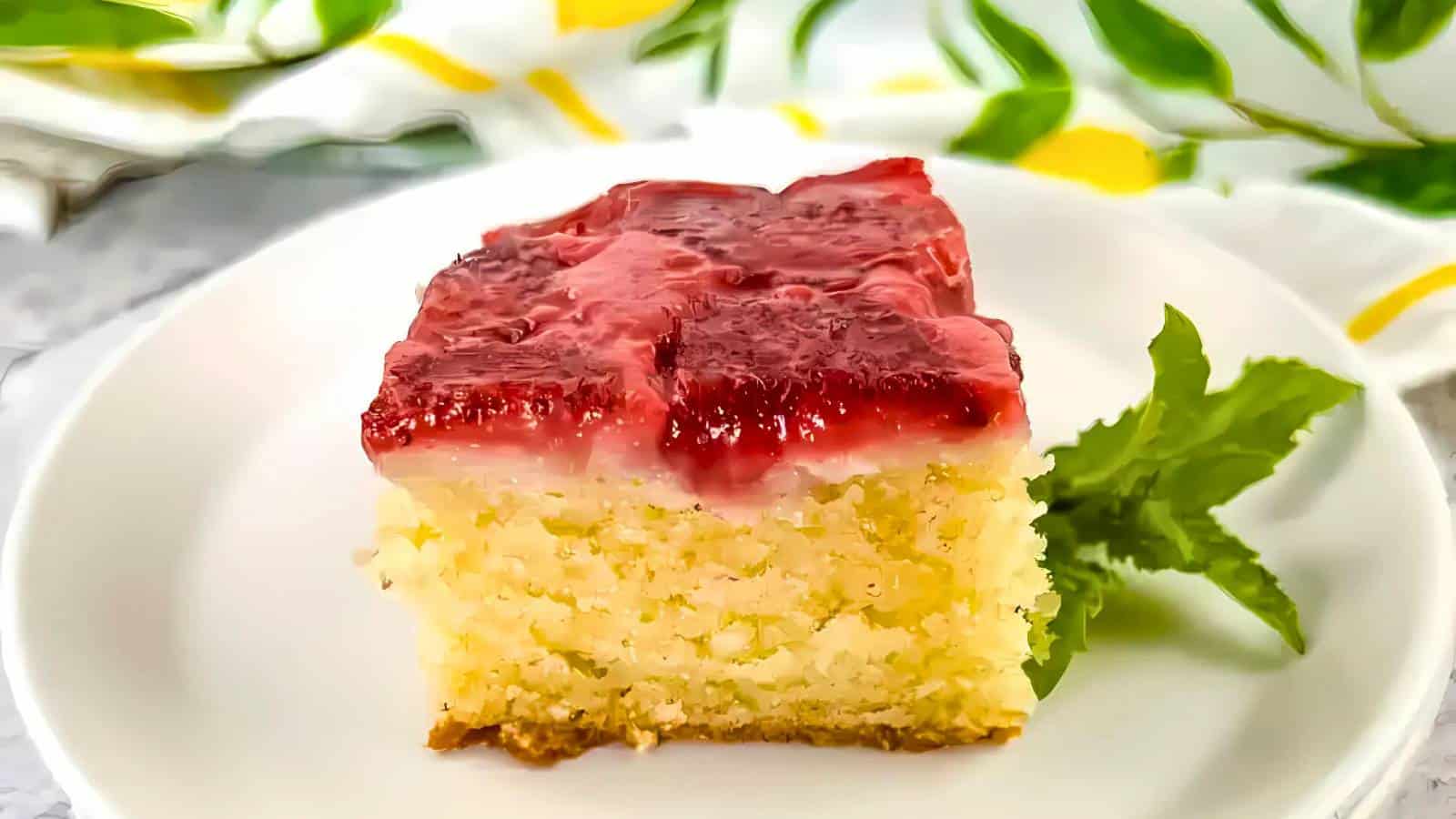 A piece of cake with a red strawberry topping on a white plate, garnished with a sprig of mint.