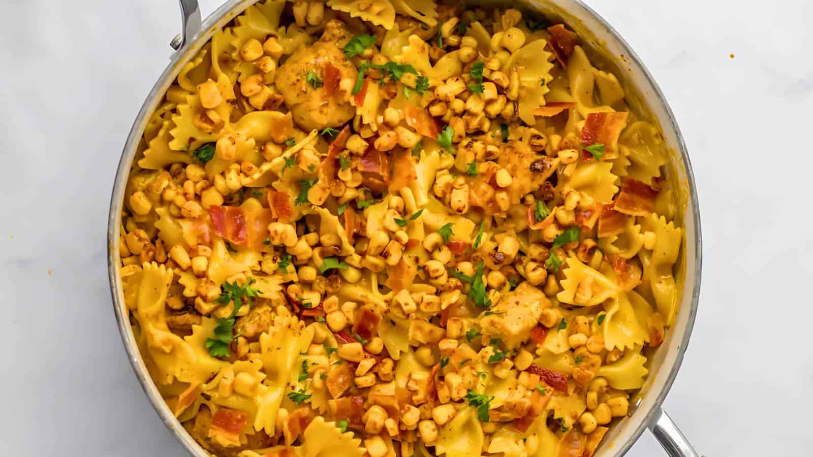 Pasta dish with bowtie pasta, corn, diced chicken, and chopped herbs in a creamy sauce, served in a metal pan.