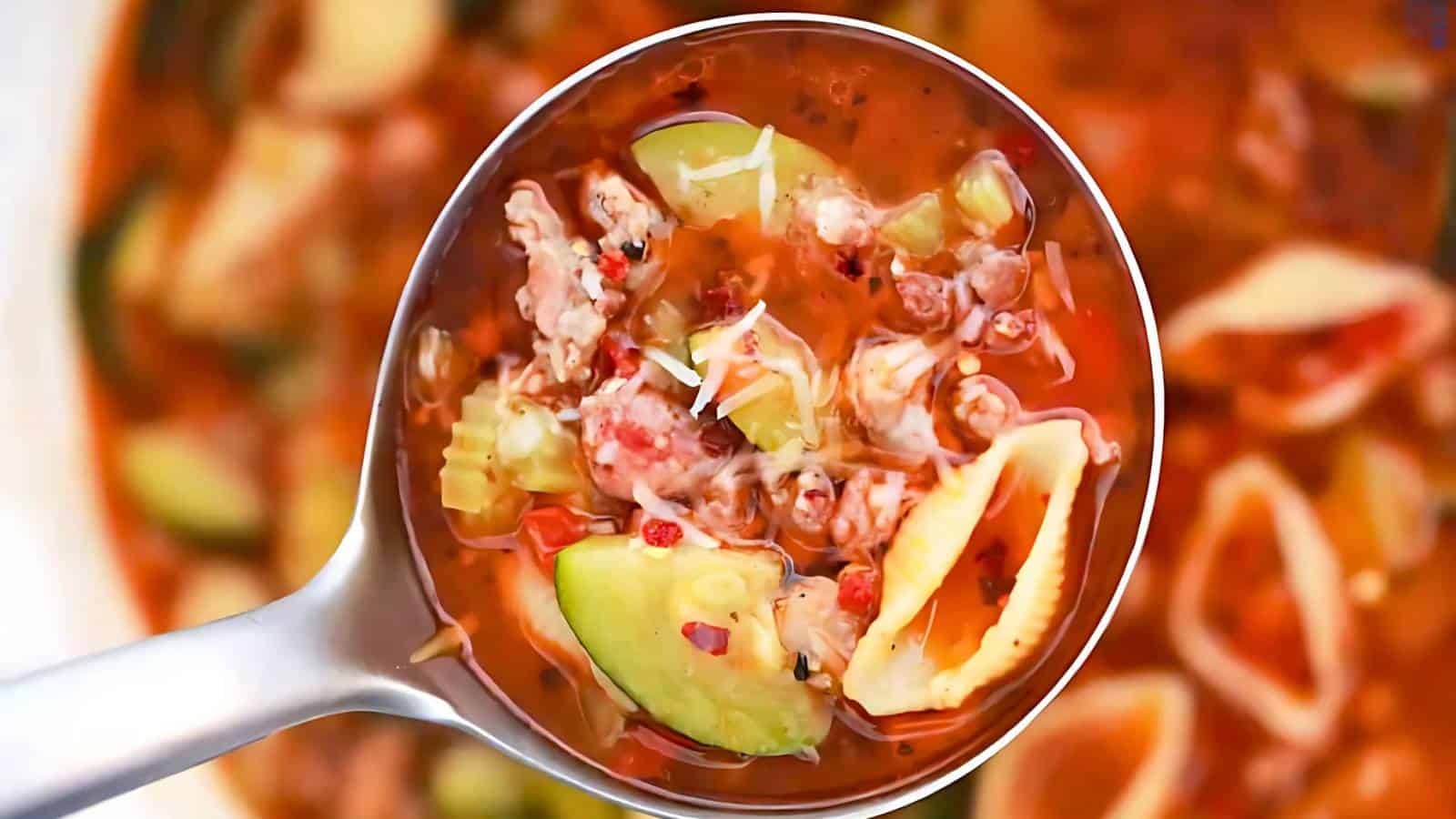 Ladle of soup with pasta shells, ground meat, zucchini slices, and tomato broth.