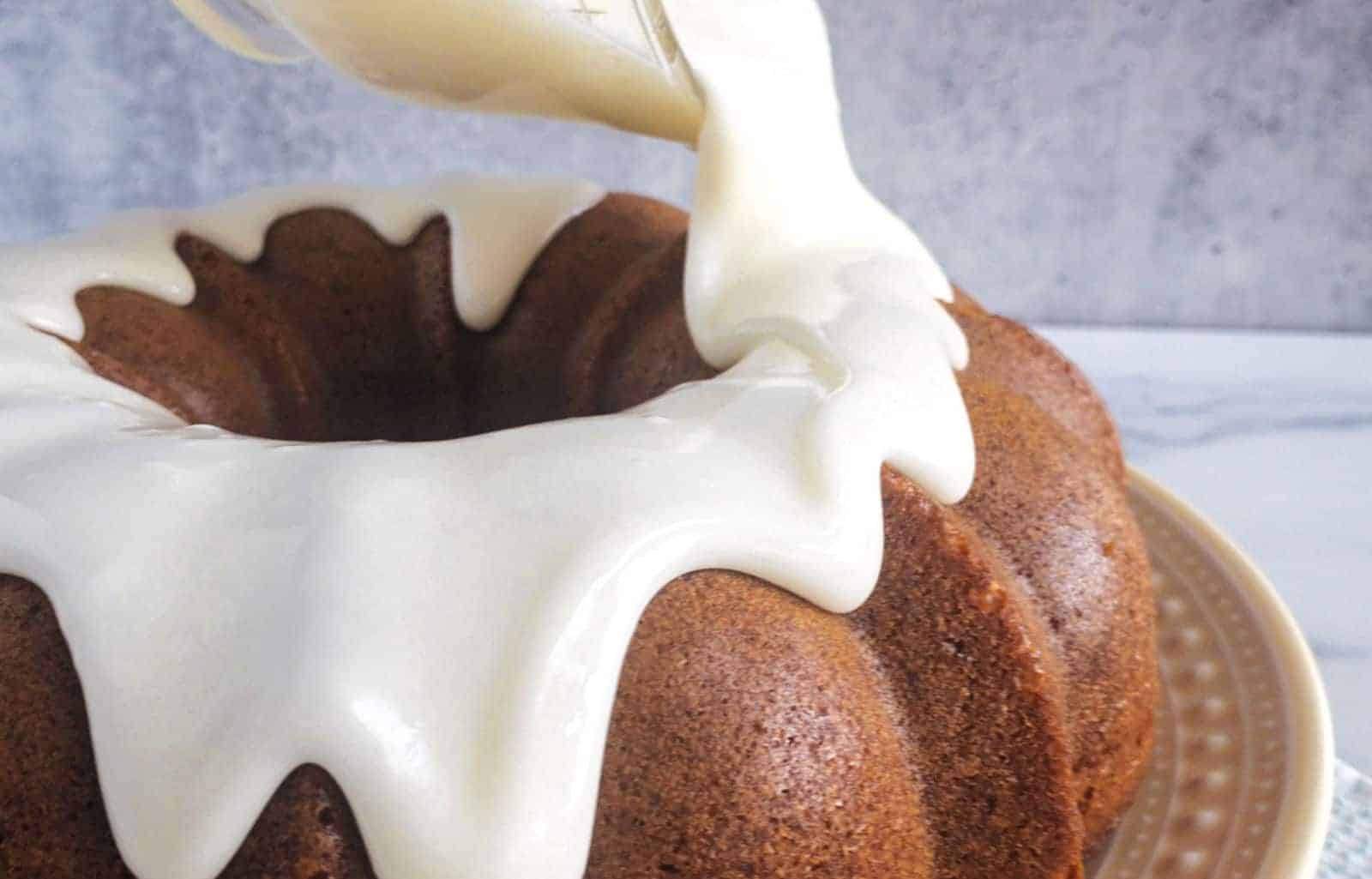 Icing being poured over a bundt cake on a plate, with a gray background.