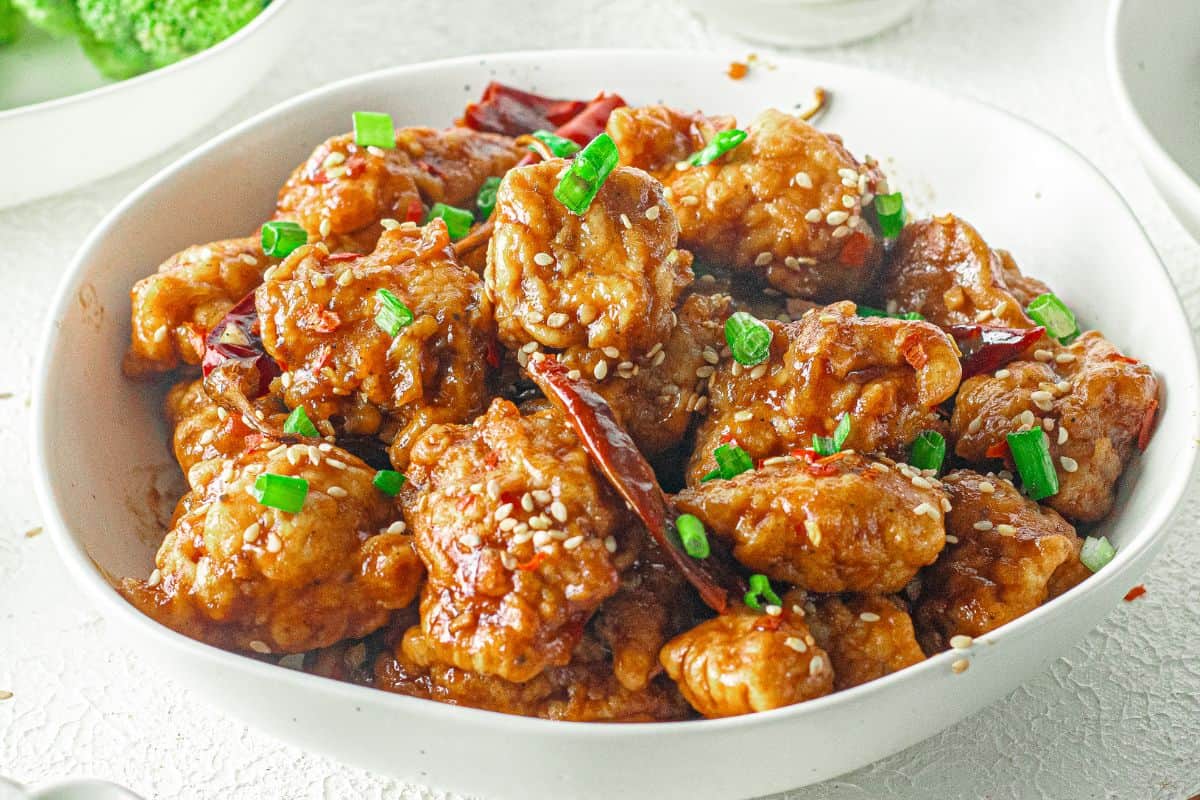 General Tso chicken in a bowl with chopsticks and green onions.