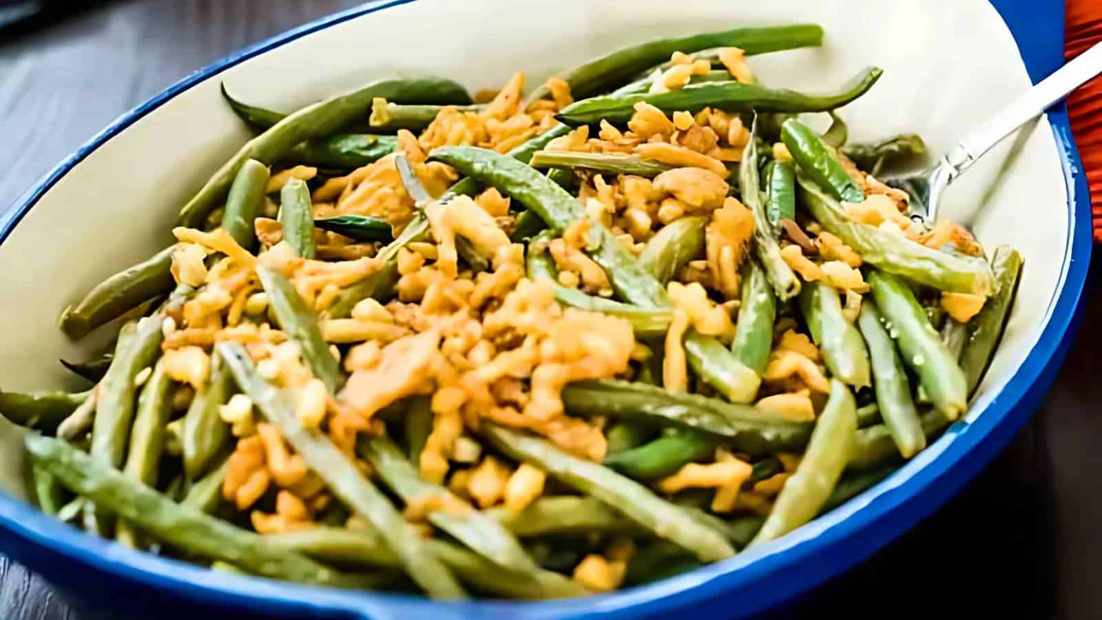 A serving dish filled with green beans topped with crispy fried onions and shredded cheese, with a fork resting on the side.