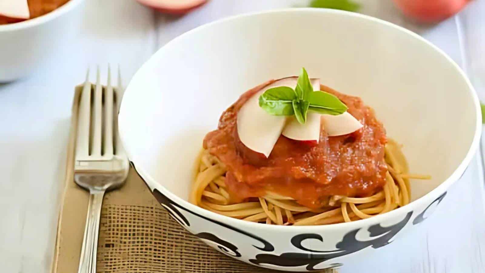A bowl of spaghetti topped with tomato sauce, sliced radish, and a basil leaf, placed next to a fork on a napkin.