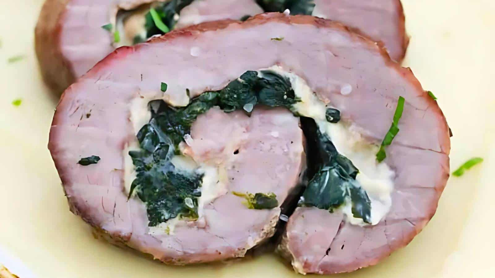 Two slices of rolled, cooked meat filled with spinach and melted cheese are shown on a plate.