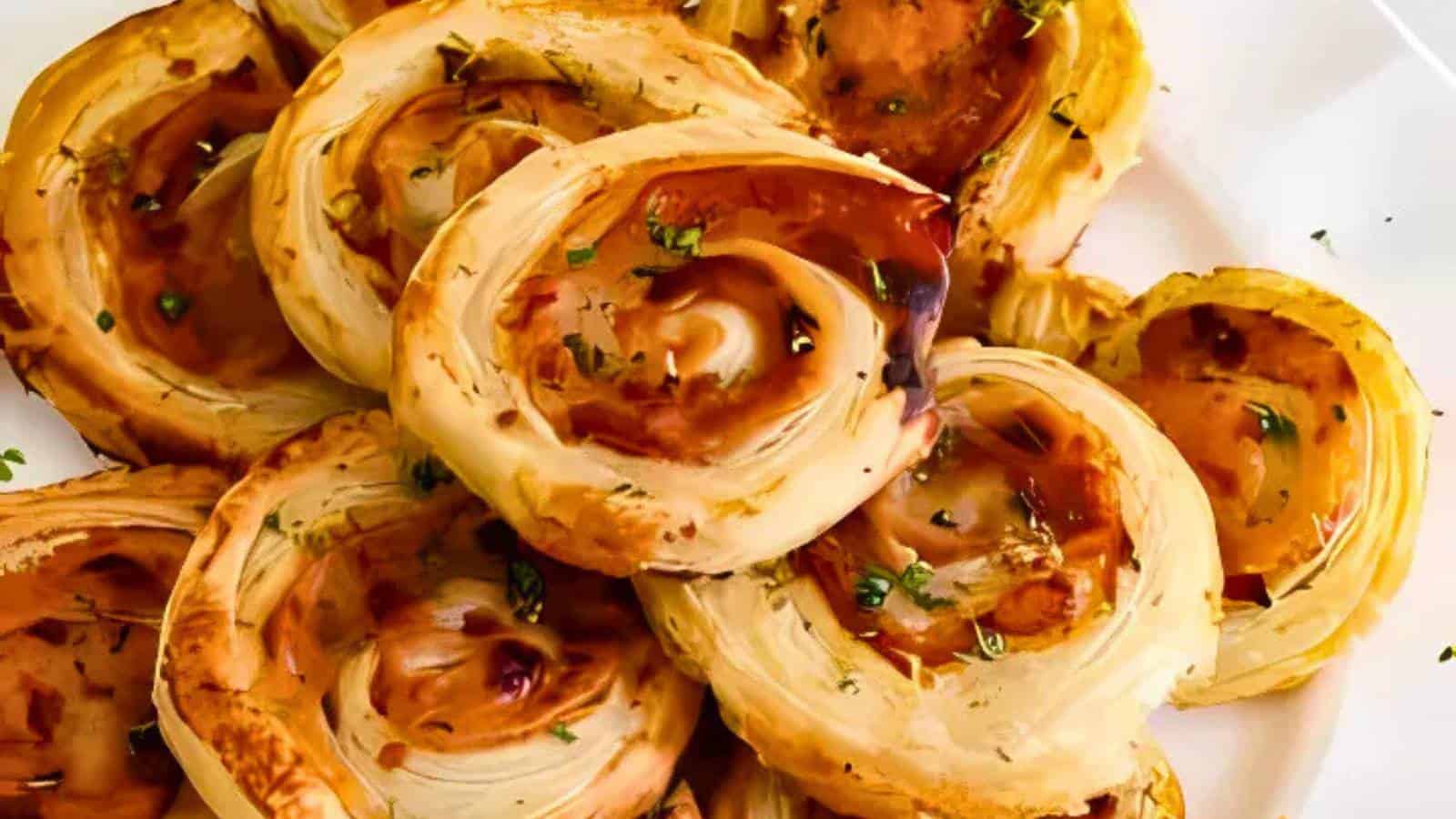 A plate of golden-brown puff pastry pinwheels garnished with herbs, arranged in a pile on a white surface.