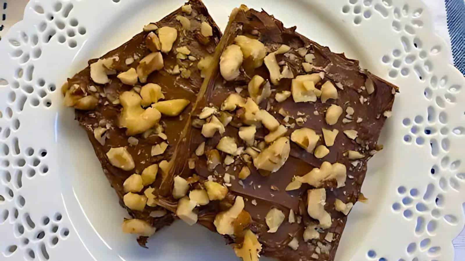 Two chocolate toffee bars topped with chopped nuts are placed on a white decorative plate.