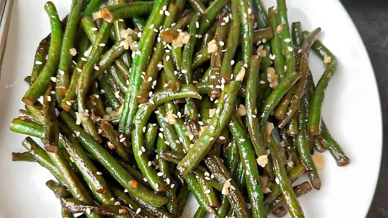 A plate of sautéed green beans garnished with sesame seeds and minced garlic.
