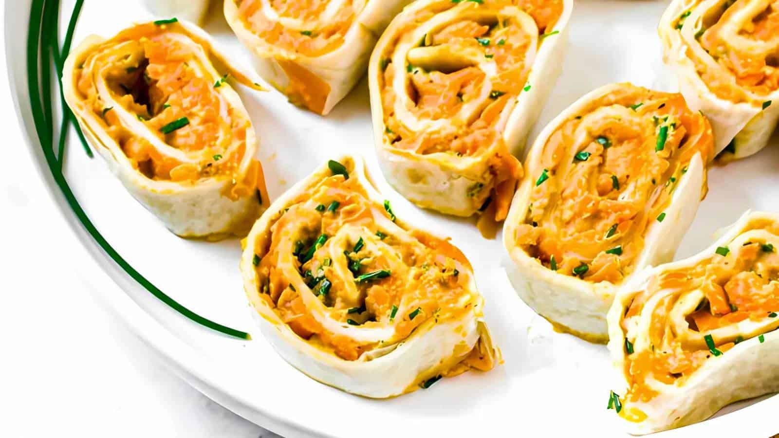 Plate of rolled tortilla pinwheels filled with orange cheese mixture, garnished with chopped herbs.