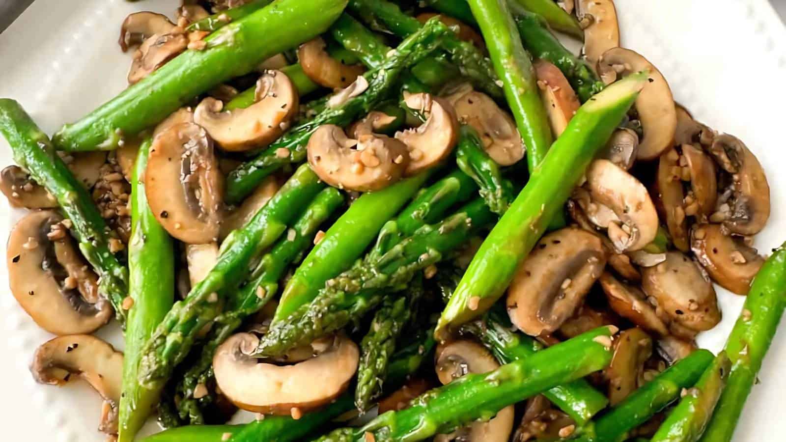 A plate of sautéed asparagus and sliced mushrooms, seasoned with sesame seeds and black pepper.