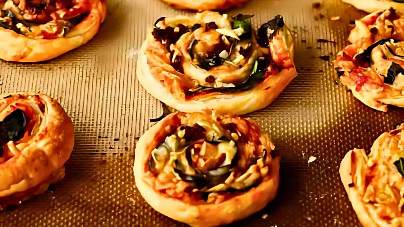 Close-up of several baked pinwheel pastries filled with vegetables and cheese, arranged on a textured baking sheet.