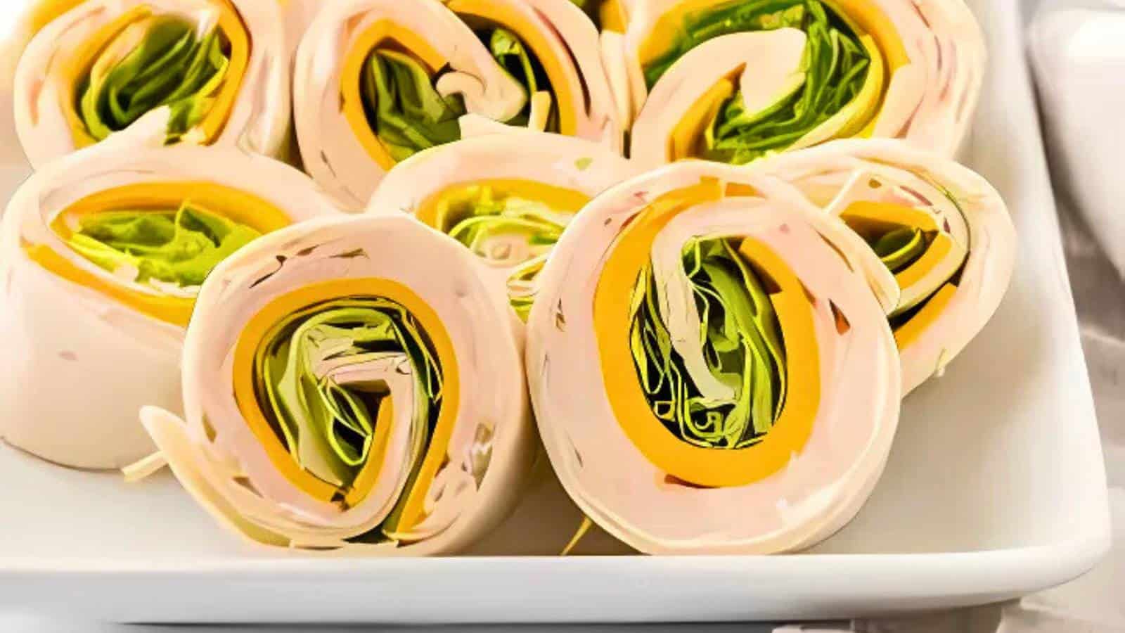 A plate of turkey, cheese, and lettuce pinwheel wraps arranged in a white dish.