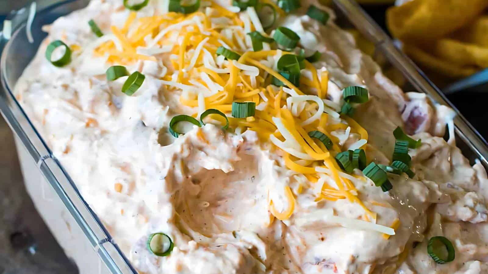 A rectangular dish filled with creamy dip, topped with shredded cheese and sliced green onions.