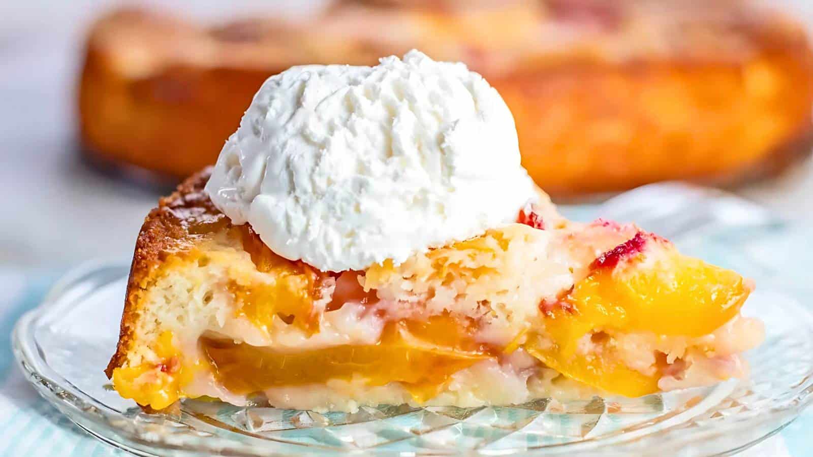 A slice of peach cobbler topped with a scoop of whipped cream sits on a clear glass plate.