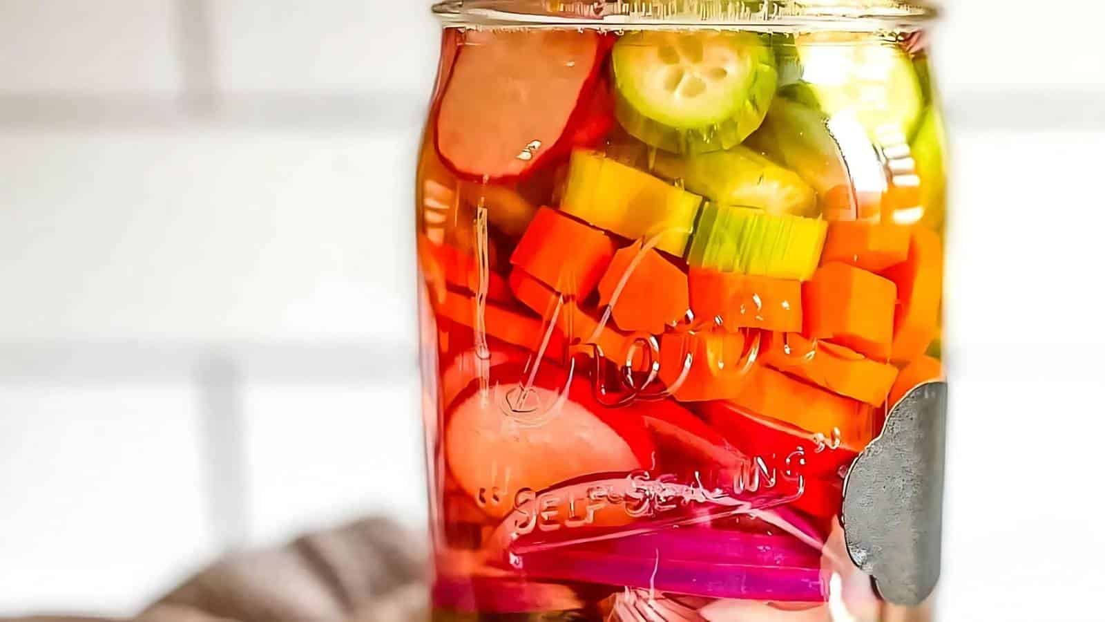 A glass jar filled with assorted pickled vegetables, including carrots, cucumbers, radishes, and onions, in brine.