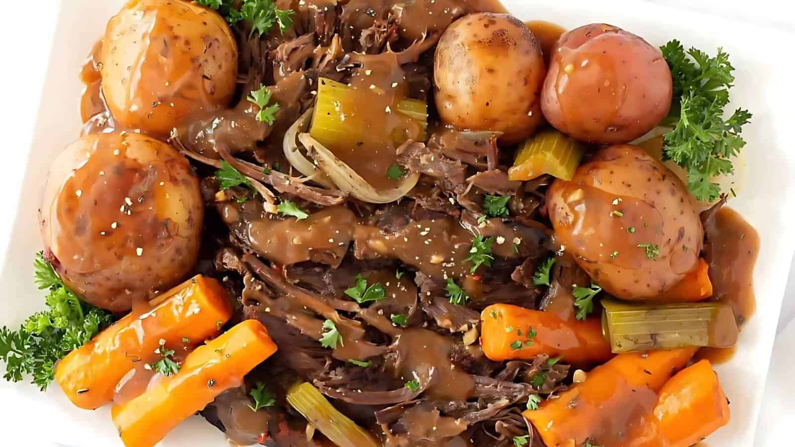 A plate of pot roast with brown gravy, surrounded by whole potatoes, carrots, celery, and garnished with parsley.