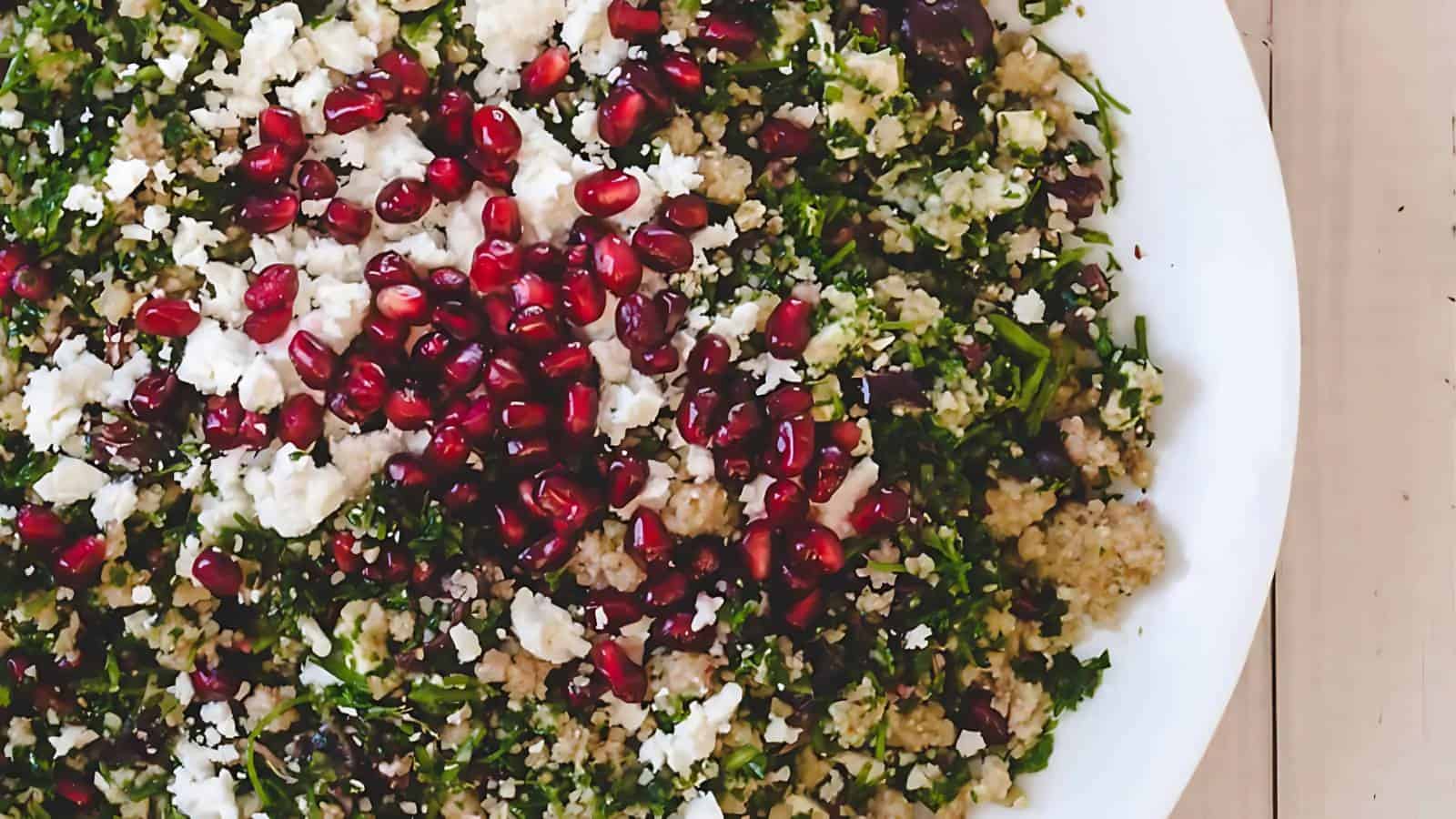 A plate of tabbouleh salad topped with crumbled feta cheese and pomegranate seeds, shown from above.
