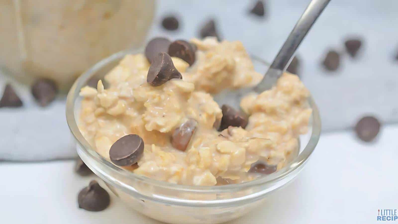 A small glass bowl of oatmeal mixed with chocolate chips, with a spoon inserted into the oatmeal.