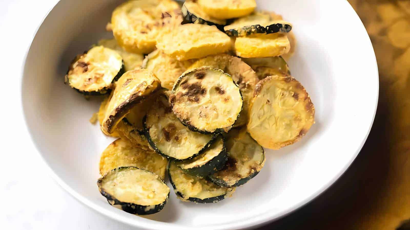 A white bowl filled with round slices of roasted or baked zucchini, some with browned edges.