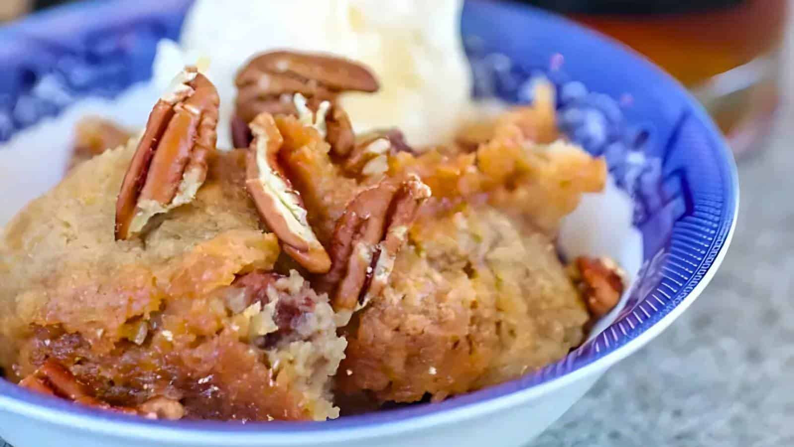 A bowl containing a serving of bread pudding topped with pecans, with a scoop of vanilla ice cream in the background.