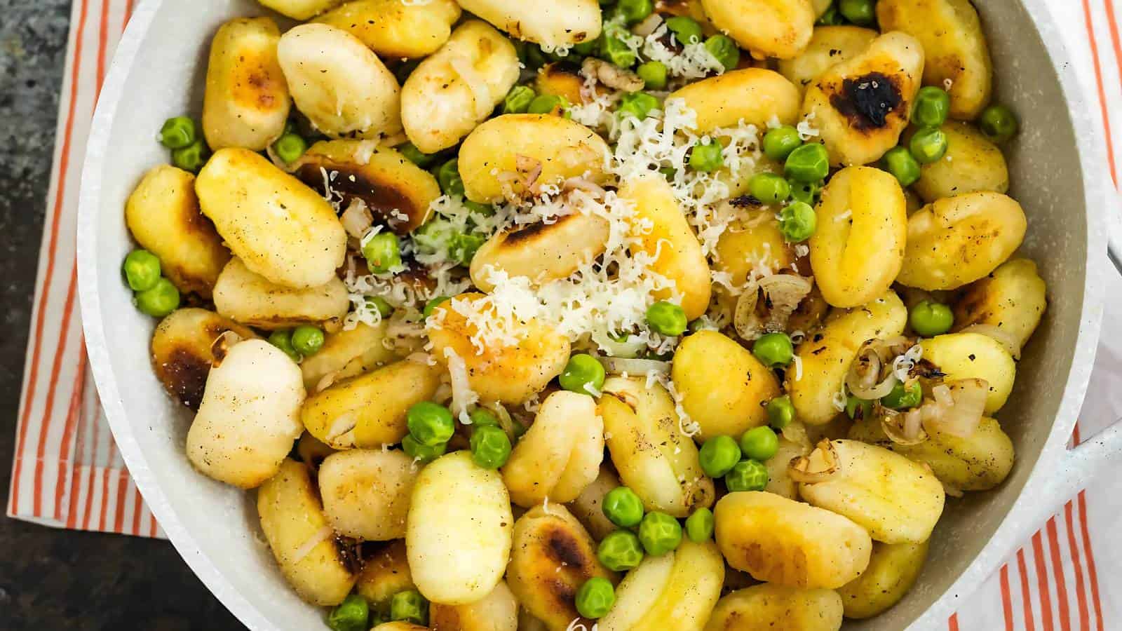 Pan of browned gnocchi mixed with green peas and topped with grated cheese, shown from above.