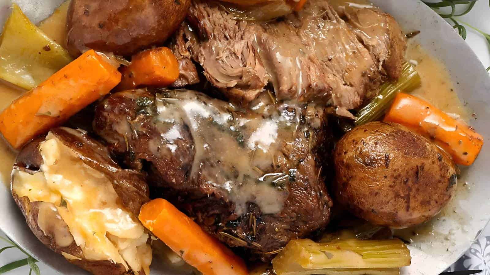 A plate of pot roast with slices of beef, whole potatoes, carrots, celery, and gravy.