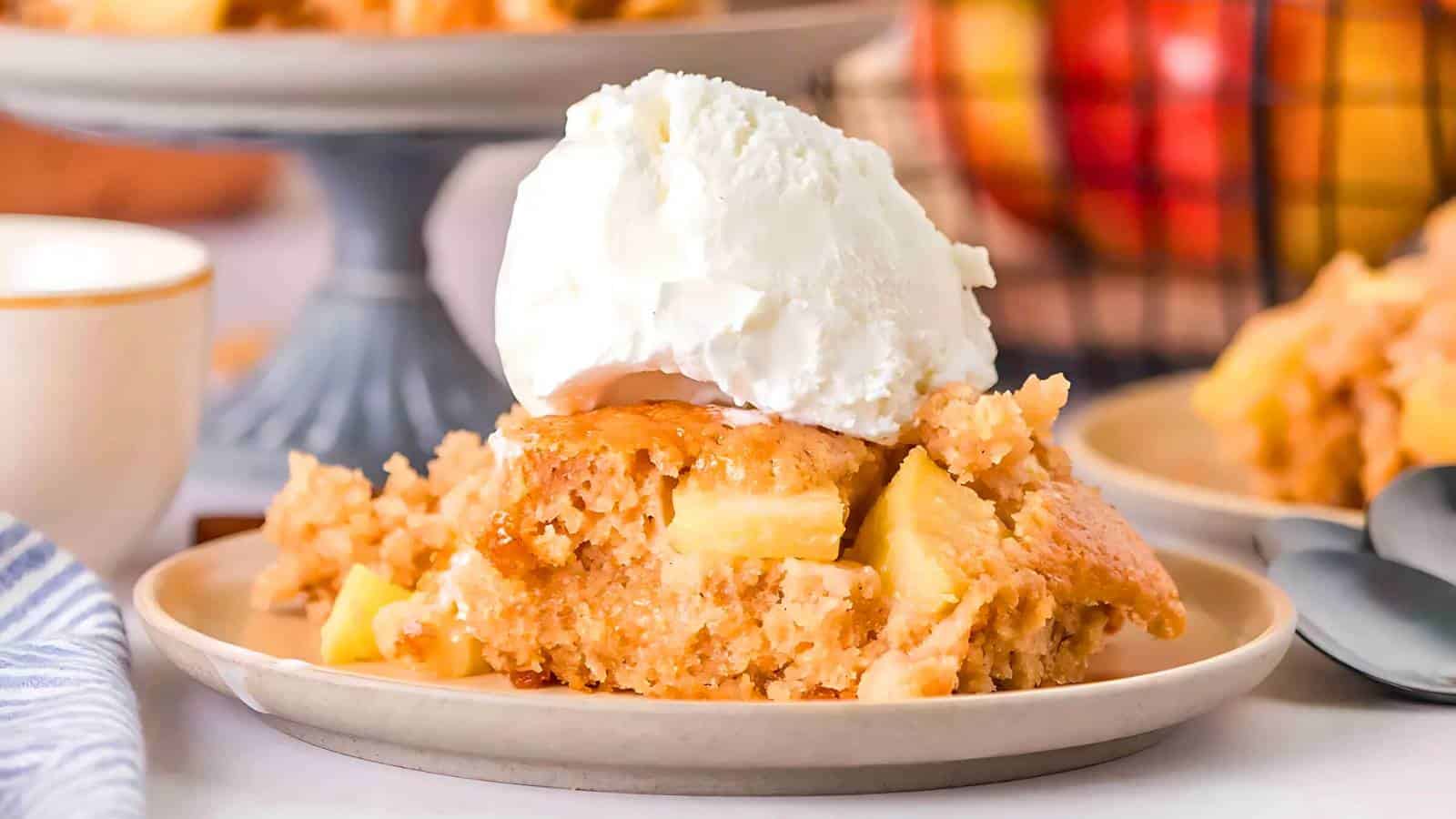 A slice of apple cobbler topped with a scoop of vanilla ice cream is served on a plate with a fork beside it.