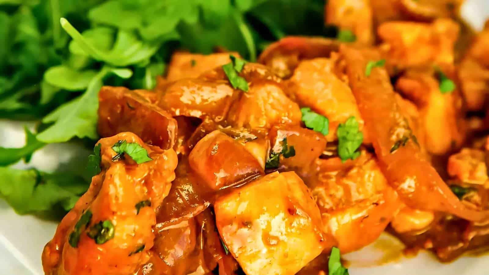 Close-up of a plate with creamy orange curry chicken garnished with chopped herbs, served alongside fresh green arugula leaves.