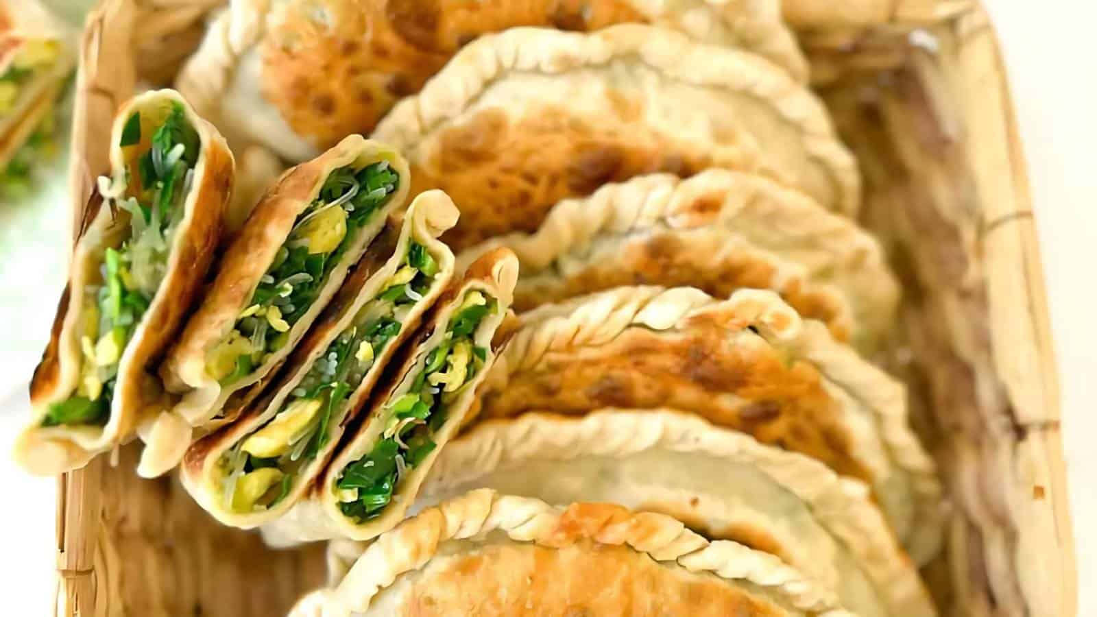 Several fried turnovers filled with chopped green vegetables and placed in a wicker basket, with a few cut open to show the filling.