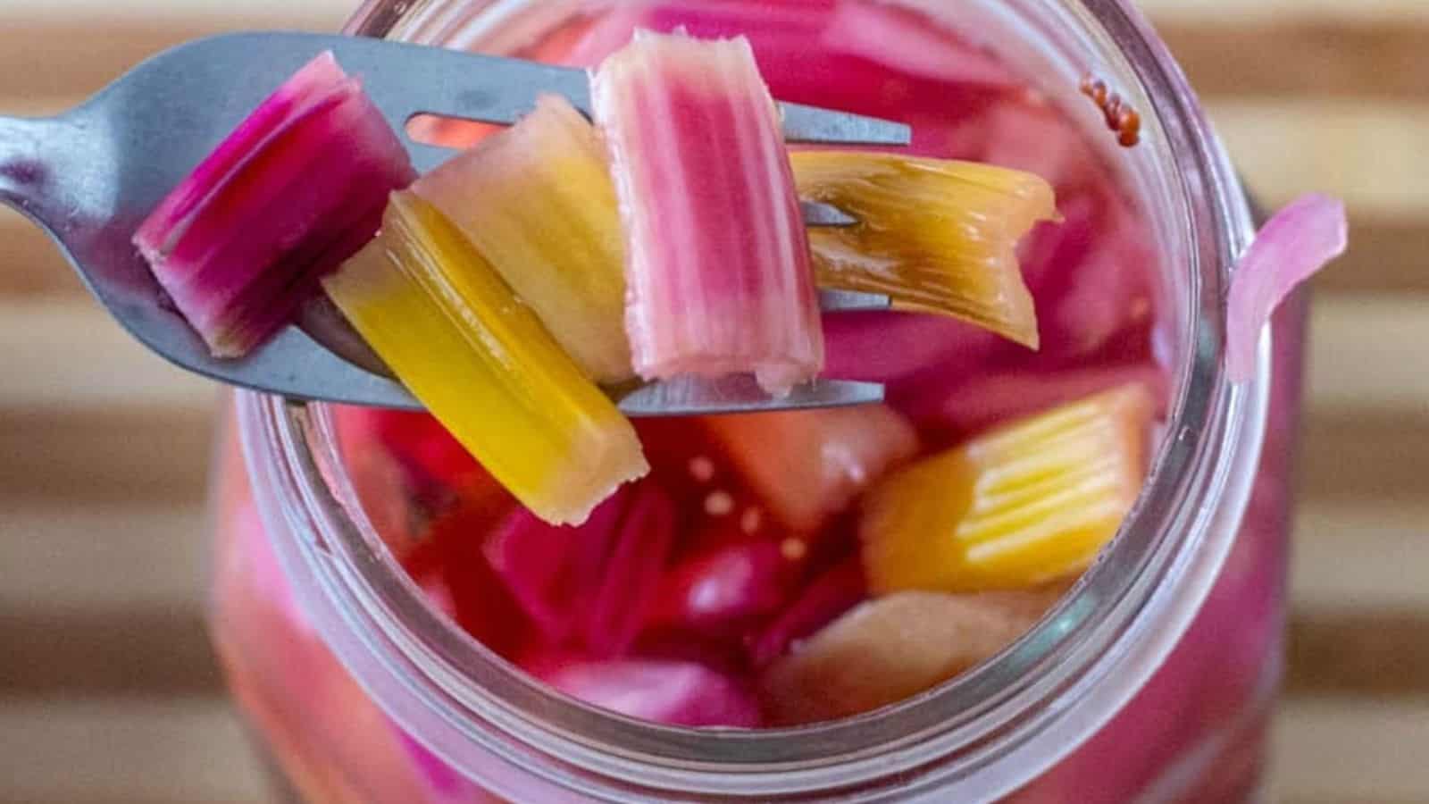 A fork holds pieces of colorful pickled vegetables above an open jar filled with similar pickled pieces.
